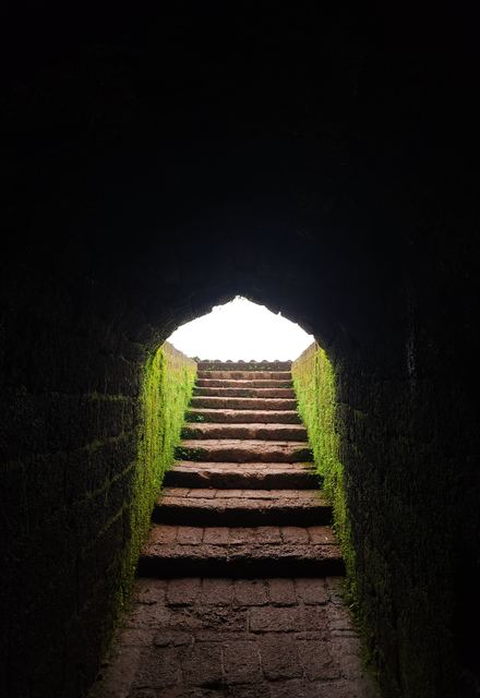 Stone steps climbing through a dark tunnel toward daylight