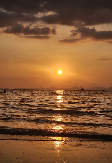 A golden sunset over the sea with a sailboat on the horizon